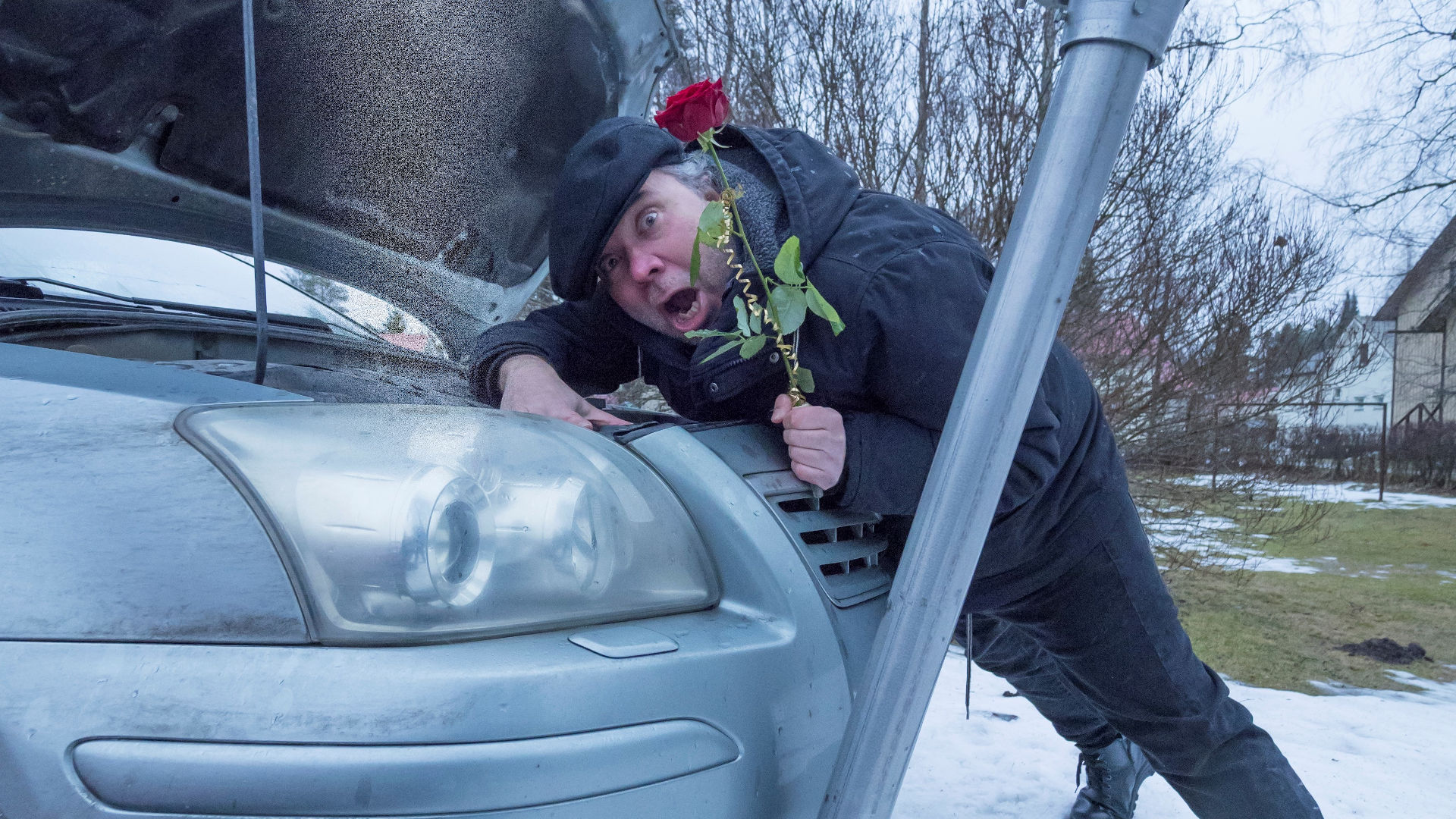 Taiteilija Henry Räsänen ilmeilee auton äärellä punainen ruusu kädessään